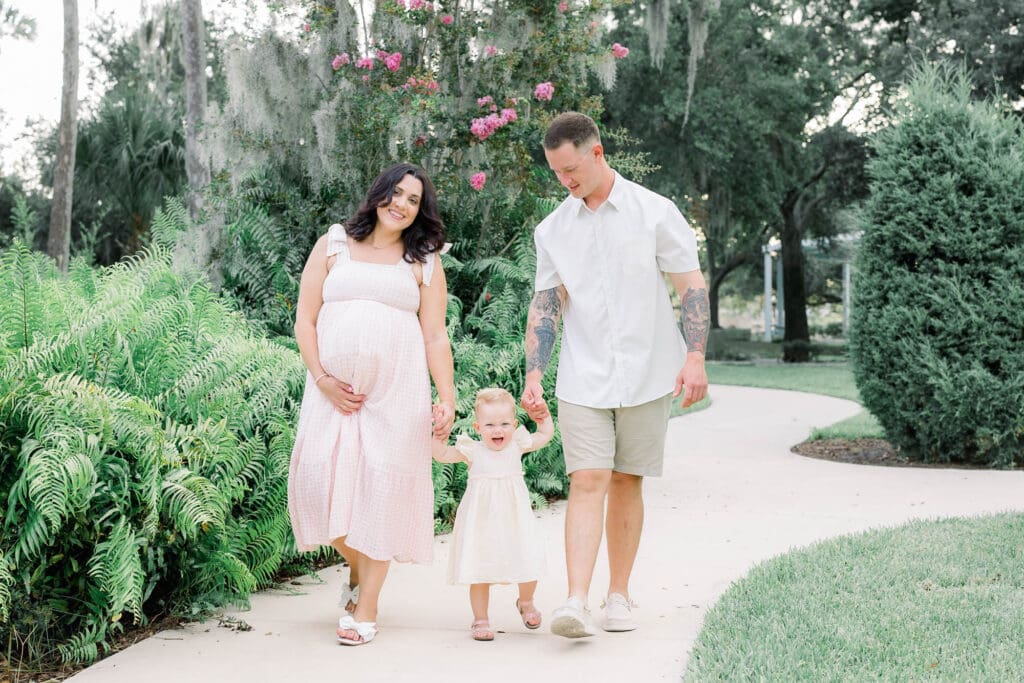 Mom experiencing a natural pregnancy after an IVF pregnancy walking with toddler and husband in Sims Park for a Tampa Maternity Photography Session.