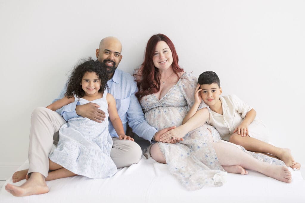 Family posing together seated on a bed during professional maternity photoshoot in Tampa.
