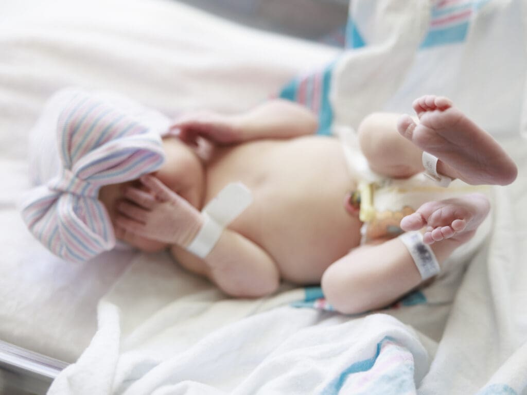 Newborn baby in hospital hat with bow, unswaddled during Tampa newborn fresh 48 photography session.