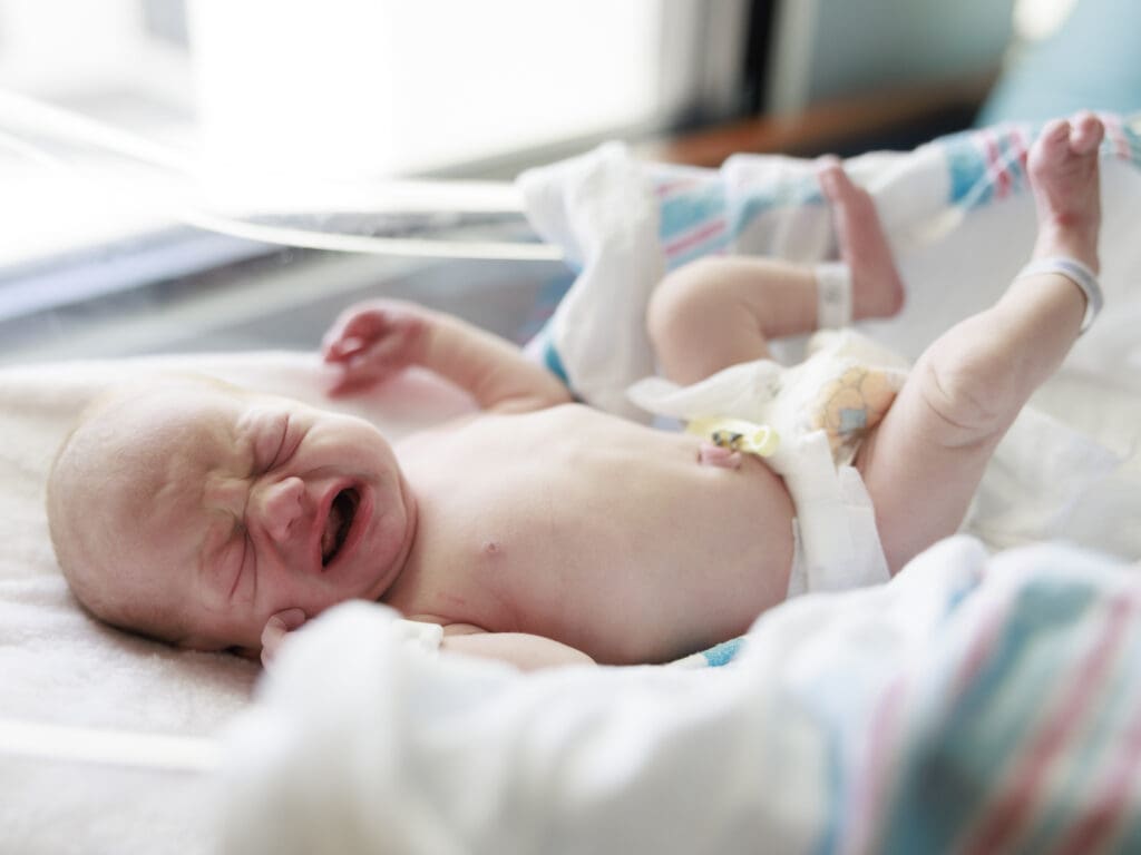 Crying newborn baby unswaddled during Newborn Fresh 48 photography session in Tampa.