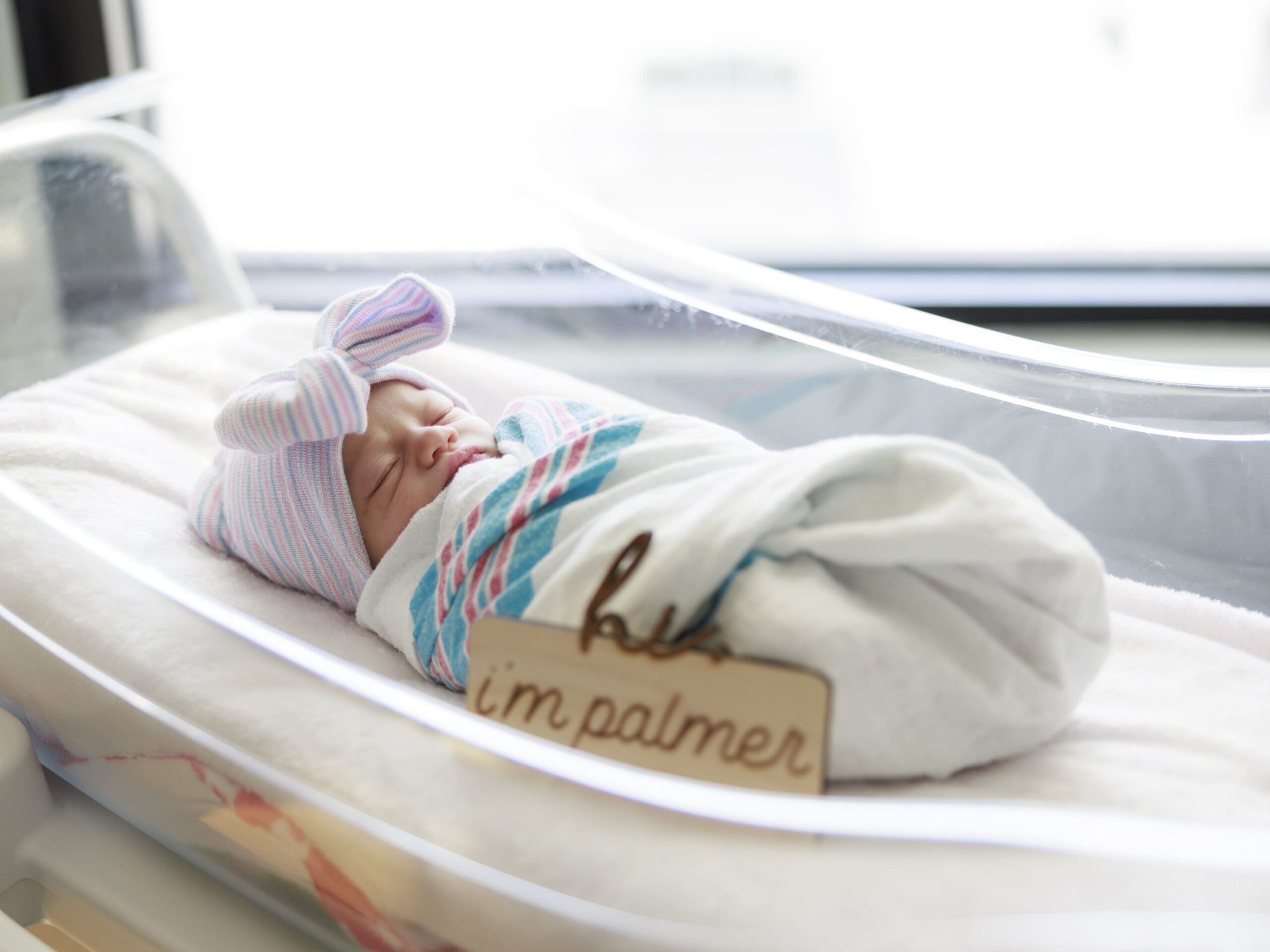 Newborn wearing hospital hat with bow and swaddled in hospital blanket during a Tampa Newborn Fresh 48 photo session.