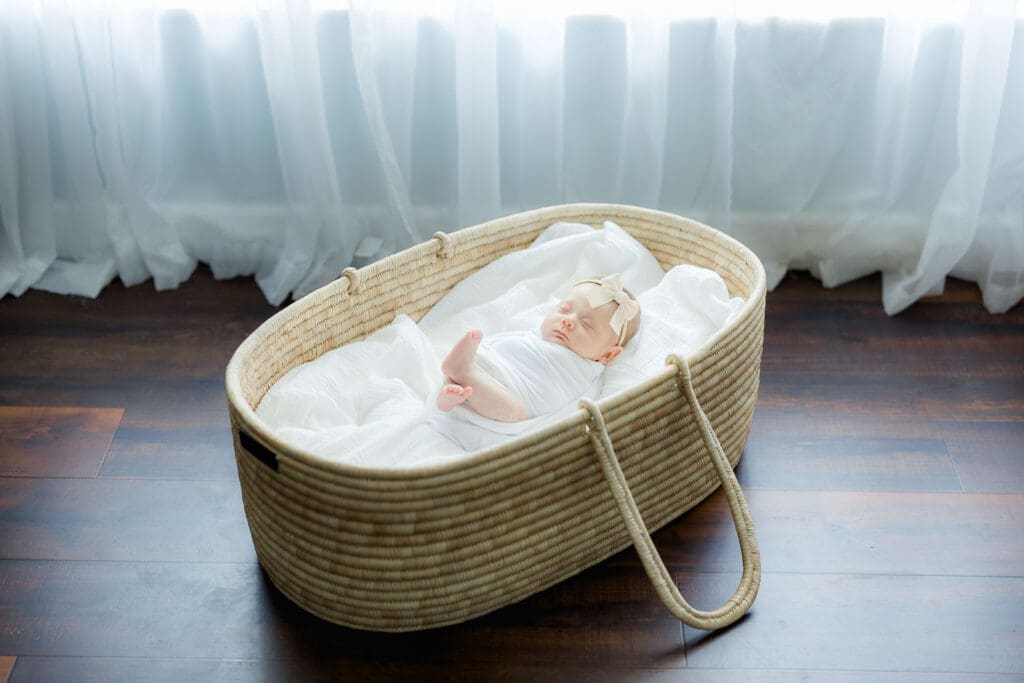 Baby girl swaddled in a white blanket sleeping in a moses basket for an in-home newborn photography session in Tampa.