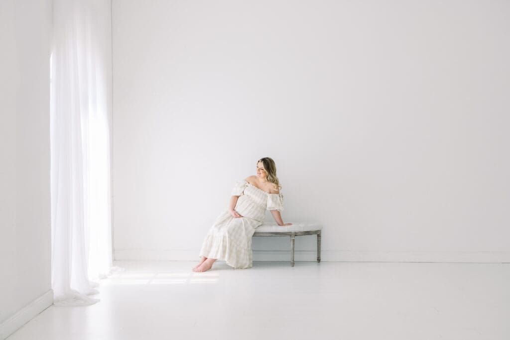 Beautiful pregnant woman sitting on a and looking out the window during a studio maternity photo session in Tampa.