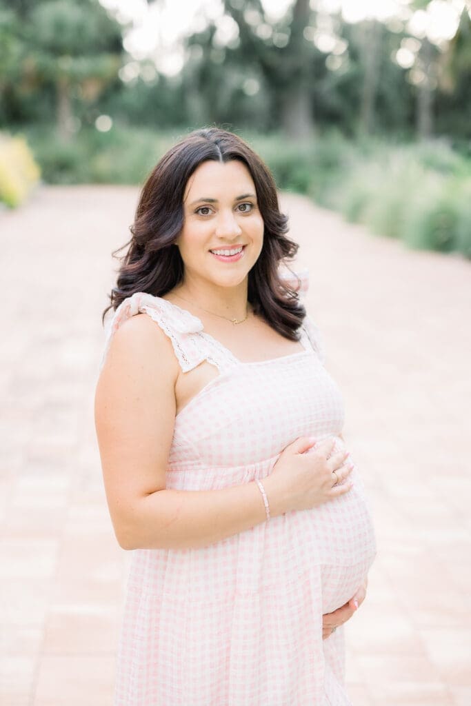 Mom experiencing a natural pregnancy after an IVF pregnancy holding belly in pink dress at Sims Park for a Tampa Maternity Photography Session.