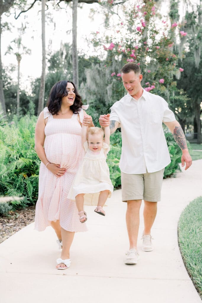 Mom and dad experiencing a natural pregnancy after an IVF pregnancy swinging toddler in Sims Park for a Tampa Maternity Photography Session.