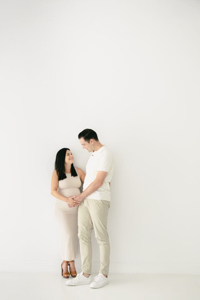 Mom and dad sharing a quiet moment during a Tampa maternity session while their toddler plays nearby with an aunt.